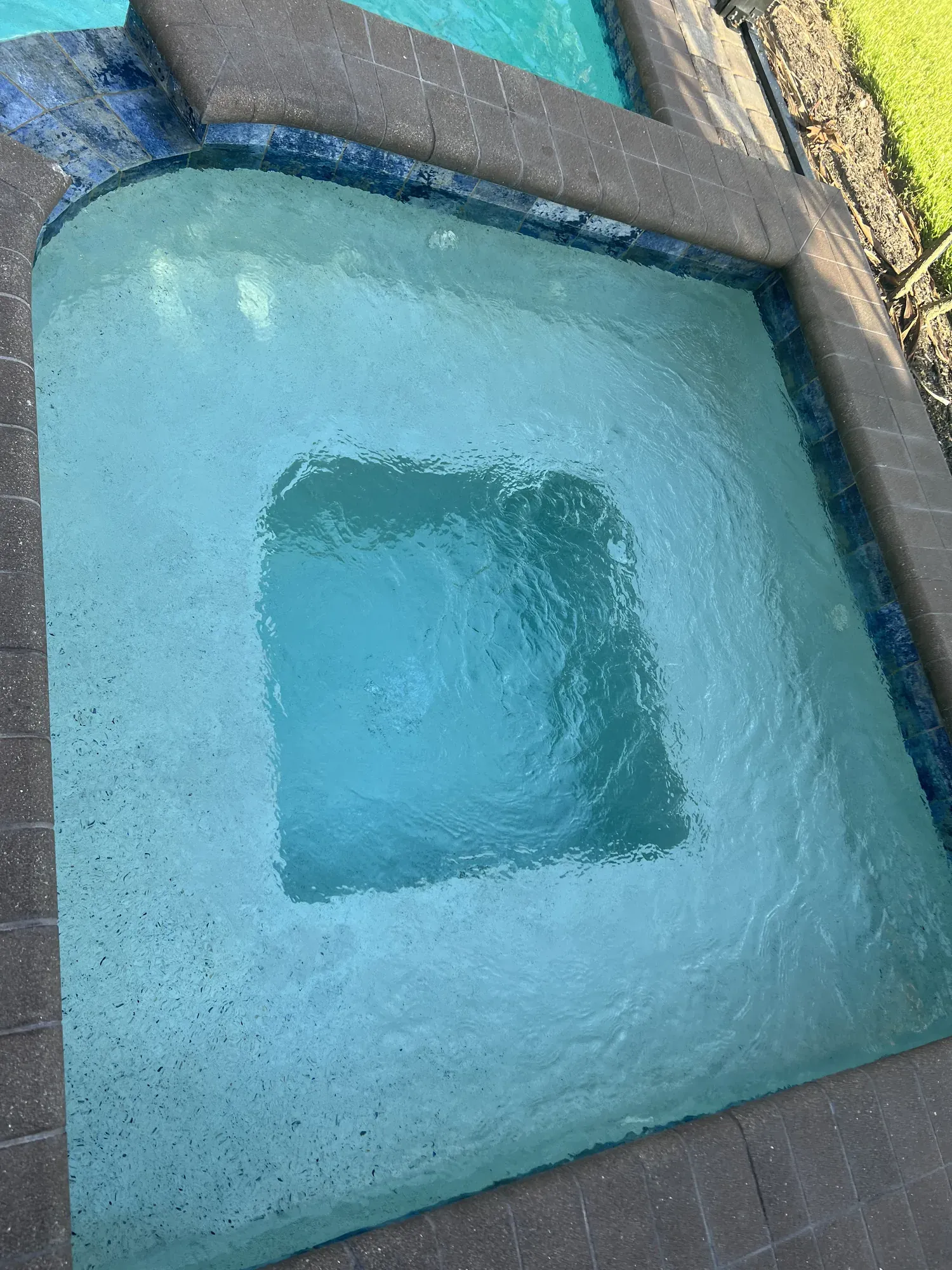 Residential spa with blue waterline tile and paver deck