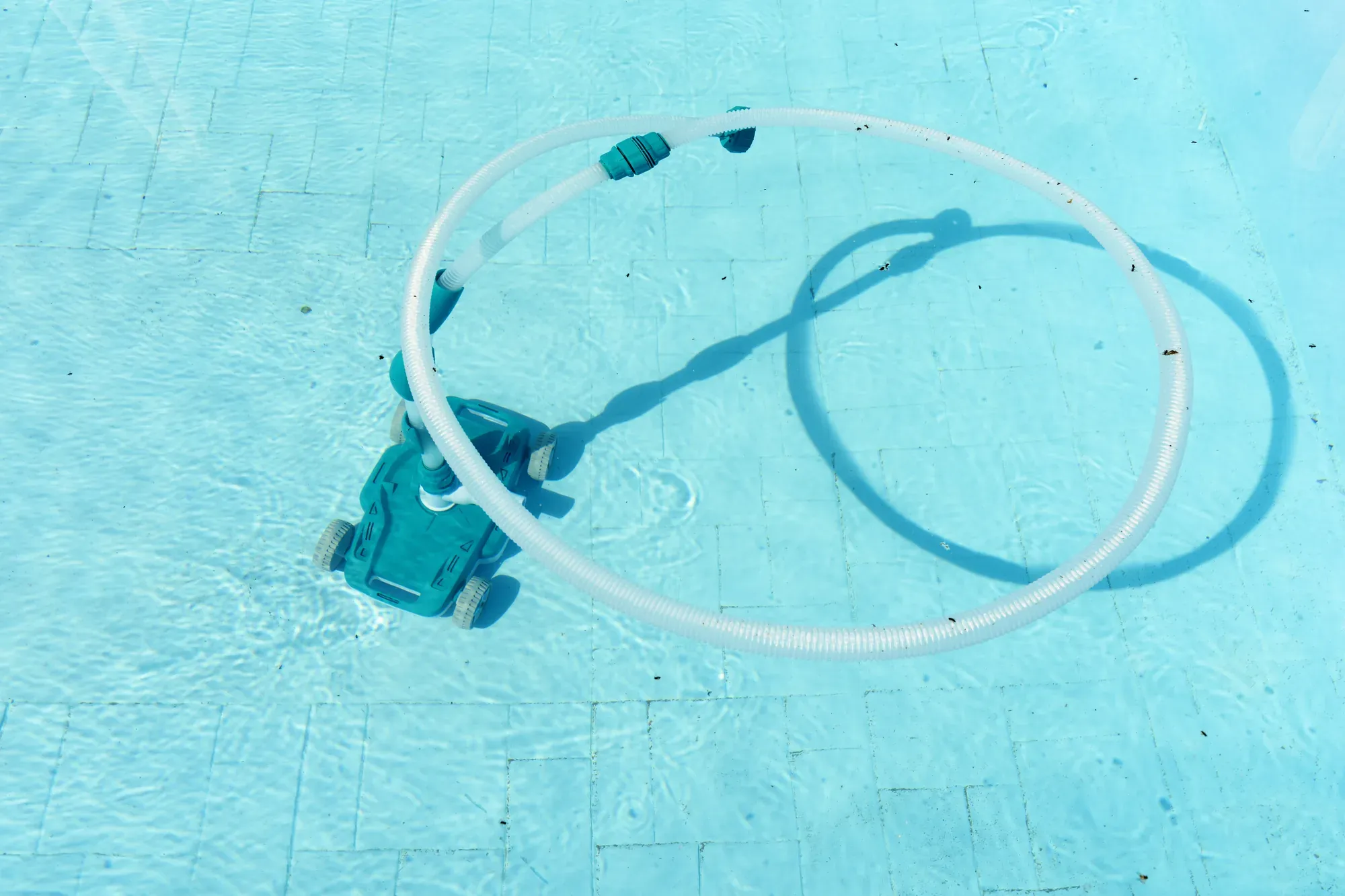Pool robot vacuum with its hose on the pool floor